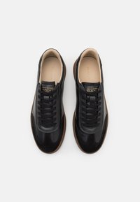 Schwarze Leder-Sneaker mit glatter Oberfläche und passenden Schnürsenkeln, ausgestattet mit einer braunen Gummisohle und dezenten Logodetails auf der Zunge.