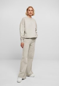 Lys beige, oversized genser med ribbestrikkede mansjetter, sammen med matchende vide bukser. Materialet ser mykt ut, med minimale sømdetaljer.