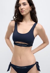 Σετ μπικίνι σε ναυτικό μπλε, με τοπ σε σχήμα scoop neck με σχ εδιασμό cut-out και λωρίδα με λογότυπο, συνδυασμένο με ψηλόμεσα σλιπ με δεσίματα.