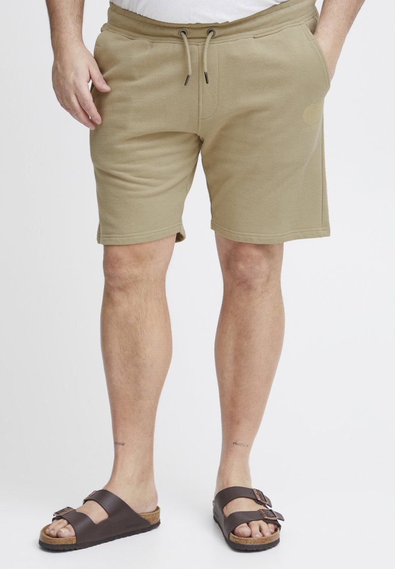 Beige cotton blend shorts with an elastic waistband and drawstring, featuring side pockets and a subtle logo on the thigh.