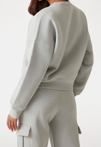 Lichtgrijze sweatshirt met een relaxte pasvorm, verlaagde schouders en geribde manchetten. Zachte textuur, minimale details en ronde hals.
