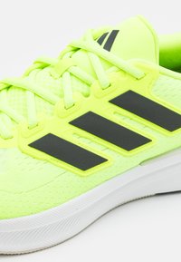 Chaussure de sport vert citron avec une tige en tricot texturé, des bandes synthétiques noires et une semelle en caoutchouc blanc avec un motif de bande de roulement.