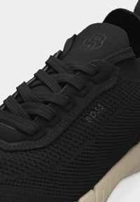 Μαύρο αθλητικό παπούτσι με πλεκτή υφή, μαύρα κορδόνια, καουτσούκ σόλα και ανάγλυφο λογότυπο "BOSS" στη πλευρά και στη γλώσσα.