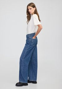 Wijd-uitlopende blauwe denim jeans met een hoge taille en voorzakken, gecombineerd met een effen witte t-shirt met korte mouwen en zwarte platformlaarzen.