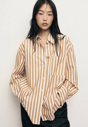 Chemise à boutons avec de larges bandes horizontales beige et blanches. Dotée d'une poche frontale, d'une coupe décontractée et d'une texture de tissu douce.