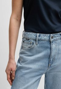 Ljusblå denimjeans med hög midja, med femficksdesign, bruna sömmar och en svart logolapp på midjebandet.