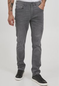 Jeans de mezclilla gris con corte ajustado, con detalles desgastados y cinco bolsillos. Combinados con zapatillas negras para un look informal.