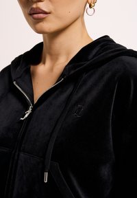 Felpa nera con zip realizzata in morbido velluto, caratterizzata da un cappuccio, zip argentata e un logo ricamato sottile sul petto.