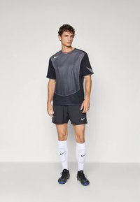 Musta ja harmaa Nike urheiluvaatesetti, jossa on lyhythihainen paita tekstuuriviivoilla, yhteen sopivat shortsit, valkoiset sukat ja mustat urheilukengät.