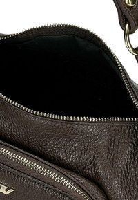 Wnętrze brązowej skórzanej torby z zamkiem błyskawicznym, charakteryzujące się teksturowaną powierzchnią i czarną podszewką, zawiera zewnętrzną kieszeń na zamek.