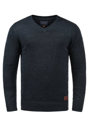 Tumši pelēks V-veida kakla džemperis, izgatavots no adīta auduma. Tam ir ribotās piedurknes un apakšmalu, kā arī neliels brūns ādas logotipa uzlīme apakšējā kreisajā stūrī.