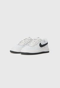 Par bijelih niskih tenisica s crnim Nike logom i crnim gumenim potplatima na bijeloj pozadini.