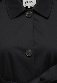 Chemise noire boutonnée avec col, en tissu sombre et lisse, dotée de deux boutons à l'avant et d'une ceinture nouée. L'étiquette indique "ONLY."