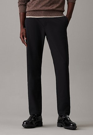 Pantaloni neri su misura con una vestibilità liscia e tagliata, dotati di tasche laterali e un design frontale piatto. Indossati con scarpe nere su uno sfondo neutro.