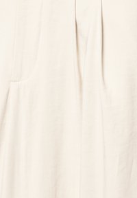 Ljust beige tyg med en slät yta, som har diskreta veck och en sidoficka. Designen är minimalistisk och utan utsmyckningar.