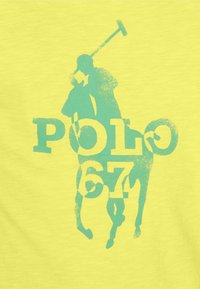 Kirkas keltainen t-paita, jossa on sininen graafinen kuva polo-pelaajasta mailan kanssa, ja teksti "POLO 67" rohkealla fontilla.