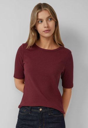 Haut à manches courtes côtelé bordeaux avec un col rond, porté sur un jean en denim foncé, présente une coupe décontractée et une texture douce.