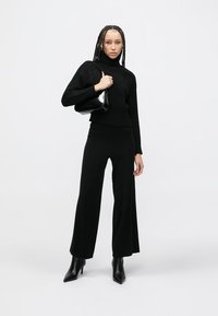 Juodas megztas aukštu kaklu megztinis su reljefiniu raštu, derinamas su plačiomis juodomis kelnėmis ir juodais aukštakulniais aulinukais. Nešiojama juoda PVC rankinė.