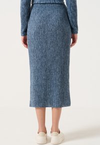 Gonna midi lavorata a maglia con texture a coste, tonalità blu, vita aderente e taglio dritto. Abbinata a scarpe da ginnastica bianche.