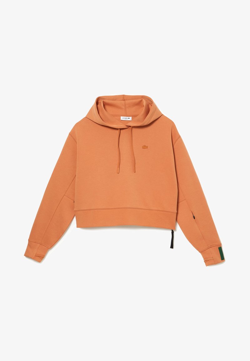 Kratší kapucí v rustikálně oranžové barvě s šňůrkou, dlouhými rukávy, malým krokodýlím logem na prsou a otvory pro palce.
