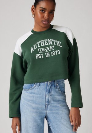 Green cropped sweatshirt with white raglan sleeves, featuring "AUTHENTIC LEVI'S EST. IN 1873" in bold text. Paired with light blue jeans.
