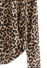 Topp med leopardmönster har en beige bas med svarta fläckar, lång ärm, en draperad sida och mjukt, strukturerat tyg.