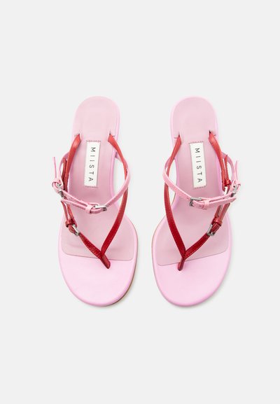 Ζευγάρι ροζ φλατ σανδάλια με λεπτά κόκκινα και ροζ σταυρωτά λουράκια και ασημένιες αγκράφες, με την ετικέτα "MIISTA" στην εσωτερική σόλα.
