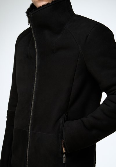 Schwarze Jacke mit hohem Kragen, gefertigt aus weichem Stoff. Verfügt über einen Frontreißverschluss und Seitentaschen, hat eine glatte Textur und ein tailliertes Design.