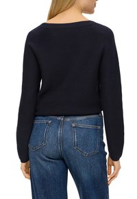 Marinblå stickad tröja med vid halsringning, figursydd silhuett och långa ärmar, tillsammans med blå denimjeans med en klassisk femfickdesign.