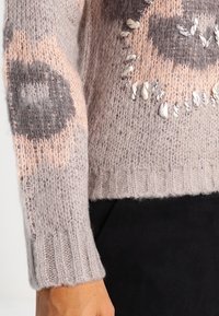 Maglione leggero in maglia di un morbido grigio chiaro, decorato con motivi rosa e grigio scuro. Presenta dettagli testurizzati e polsini a coste.