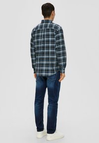 Chemise à carreaux bleus à manches longues, col boutonné et ourlet arrondi, associée à un jean en denim foncé et des baskets blanches.