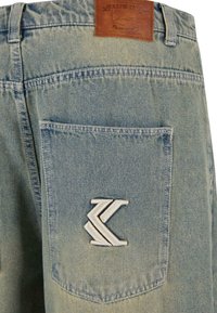 Vaaleansiniset denim-shortsit, joissa on nahkapläntti vyötäröllä ja valkoinen kirjailtu logo takataskussa. Ominaisuuksiin kuuluu kulunut pinta.