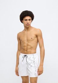 Witte zwemshorts met een elastische tailleband, een zwart trekkoord en een gedrukt logodetail aan de zijkant. Soepele textuur, knielang model.