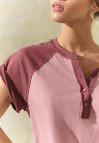 Korte mouwen henley shirt in roze en kastanjebruin, met een knoopsluiting, zachte stof en contrasterende raglan mouwen. Gladde textuur.