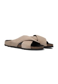 Beige suède instapsandalen met gekruiste banden en een kurken voetbed. De zool is gestructureerd voor grip. Lichtgewicht en open teen ontwerp.