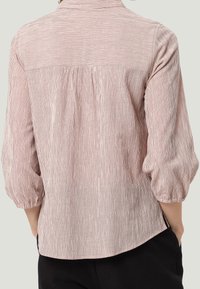 Blouse en coton rose clair à rayures, avec col boutonné, manches bouffantes et empiècement arrière froncé ; tissu texturé à lignes verticales.
