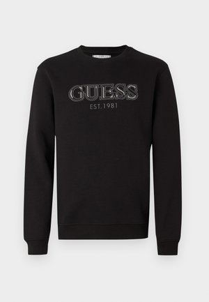 Fekete kerek nyakú pulóver hosszú ujjakkal, amelyen a mellkason kontrasztos cérnával hímezve található a "GUESS EST. 1981" felirat.
