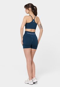 Merihenkinen urheiluliivi ja siihen sopivat shortsit joustavasta kankaasta. Ominaisuuksiin kuuluu kilpailutakaosa, logo vyötäröllä ja sileä rakenne.