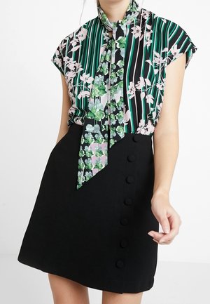 Blusa a maniche corte floreale e a righe con colletto annodato, abbinata a una mini gonna nera con bottoni decorativi lungo il lato.