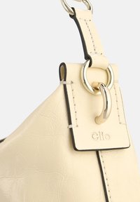 Crèmekleurige leren handtas met een getextureerde afwerking, voorzien van een ronde gouden metalen sluiting en een gestikte leren label met het reliëf "Clio."