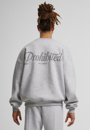 Grå sweatshirt lavet af blødt stof. Har overdreven pasform og ribbede manchetter. Viser teksten "Forbudt" og "10119 BERLIN" på bagsiden.