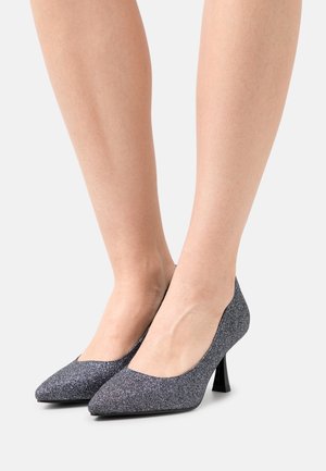 Escarpins à talons hauts gris pailletés avec un bout pointu, un empeigne basse et un talon noir brillant et fin. Texture lisse et finition scintillante.