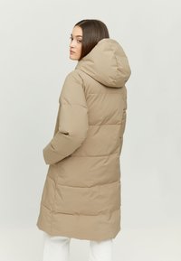 Beige padded coat with a hood, featuring a quilted design and long sleeves, shown from the back with hands in side pockets.