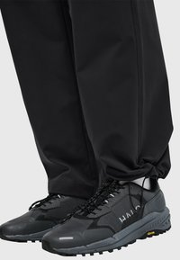 Zwarte waterdichte broek met elastische boorden, gecombineerd met grijze sneakers met mesh en rubberen materialen, gestructureerde zolen en reflecterende accenten.