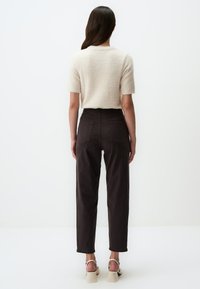 Crème kort samengestelde trui met korte mouwen van een pluizig materiaal, gecombineerd met donkerbruine, hooggelegen broek met twee achterzakken. Beige haksandalen.