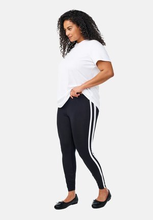 Mustat leggingsit valkoisilla sivuraitoja, yhdistetty valkoiseen t-paitaan. Ominaisuudet: istuva muotoilu ja sileä pinta, käytetty mustien flats-kenkien kanssa.