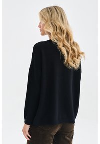 Czarny, oversize sweter z długimi rękawami, prążkowanym wykończeniem i okrągłym dekoltem; miękka tekstura; pokazany z tyłu na jasnym tle.