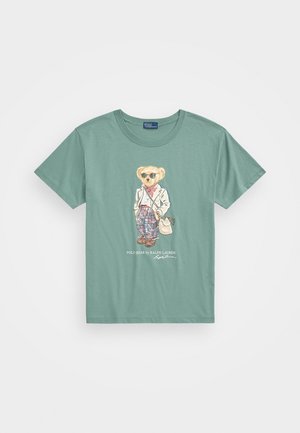 Grøn bomuld t-shirt med et cartoon-bjørn i solbriller, iført en hvid blazer, ternet bukser og holder en taske. Frontgrafikdesign.