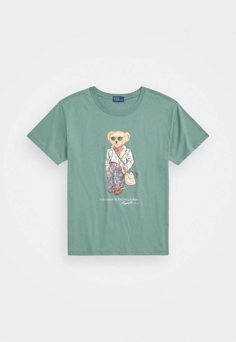 Camiseta de algodón verde con un oso de dibujos animados con gafas de sol, vistiendo un blazer blanco, pantalones a cuadros y sosteniendo una bolsa. Diseño gráfico en la parte delantera.