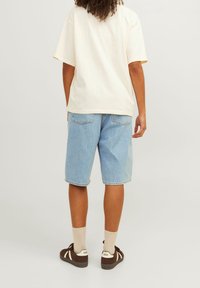 Beige oversized tričko, světlé modré džíny s rovnými nohavicemi, hnědé tenisky s krémovými akcenty a béžové ponožky.